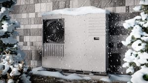 A heat pump against a wall covered with snow.